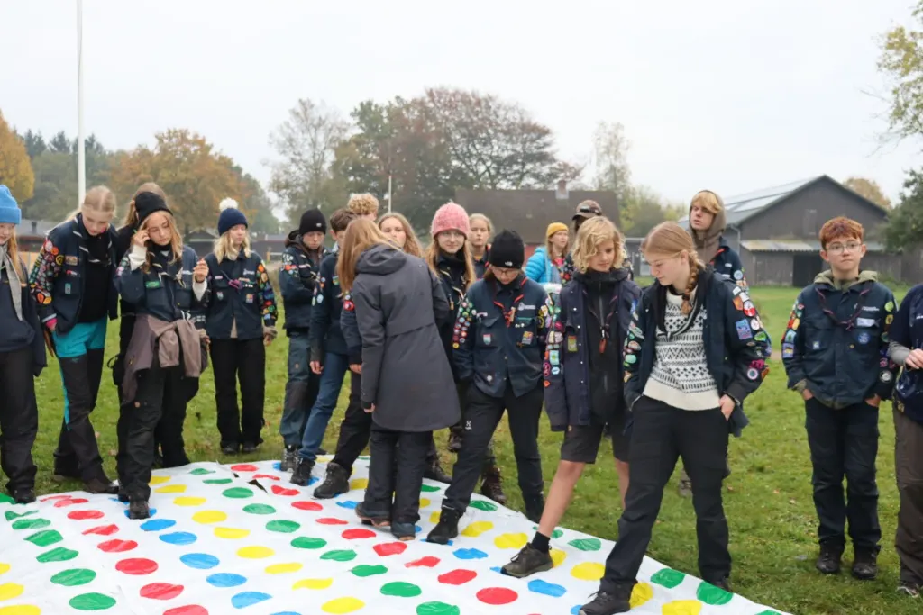 Stor gruppe spejdere leger på en kæmpe twister-plade på græsset